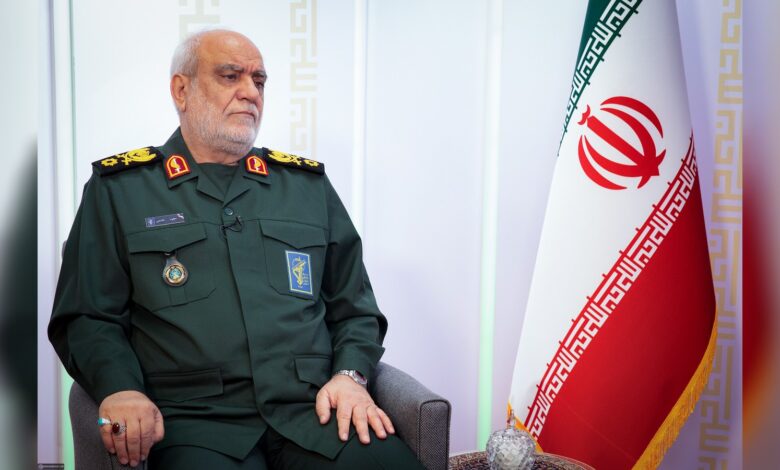 Majid Khademi seated in military uniform beside Iranian flag.