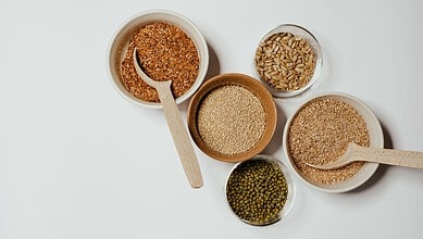 Assorted grains and seeds including millet, sesame, and green gram in bowls with wooden spoons.