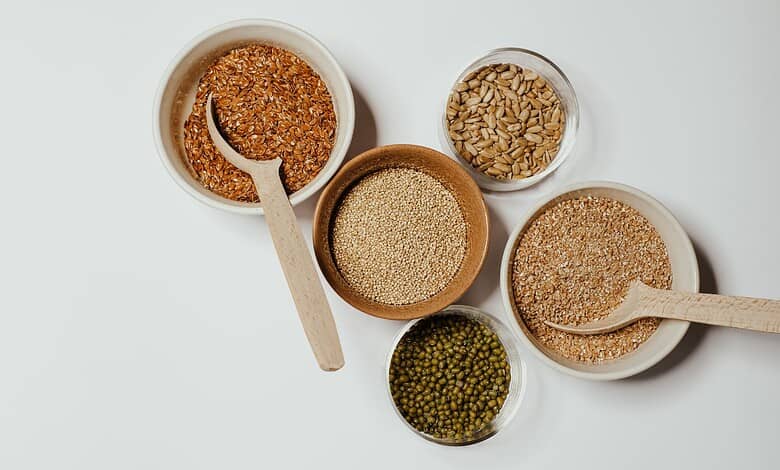 Assorted grains and seeds including millet, sesame, and green gram in bowls with wooden spoons.