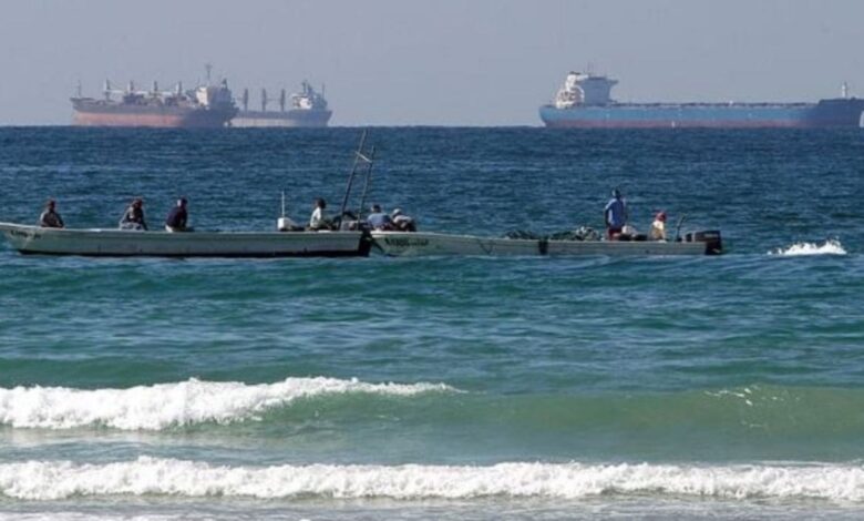 Small fishing boats near the shore with large oil tankers visible in the Strait of Hormuz.