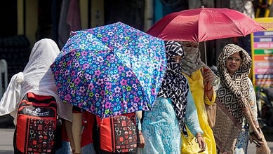 Women with umbrellas walking in a busy street, wearing traditional attire.