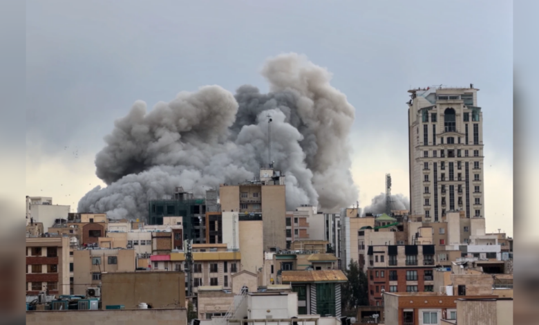 Thick grey smoke billows over buildings in Tehran after an air strike, rising above the urban skyline.