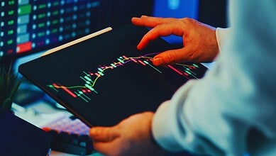 A person monitoring stock market data on a tablet, illustrating the dangers of fake trading platforms and financial fraud.