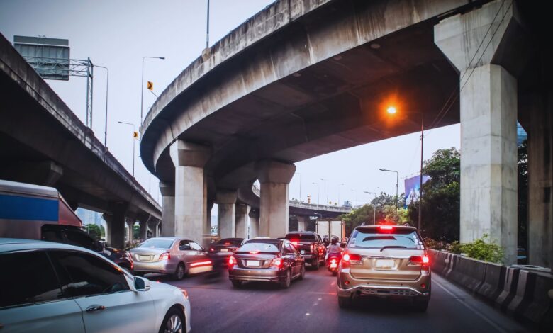 Image shows Cars stuck in heavy traffic under a multi-level concrete highway interchange at dusk.