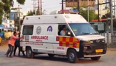 An ambulance being pushed by two people on a city street in India.