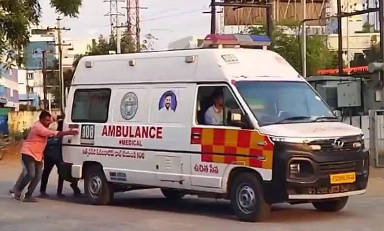 An ambulance being pushed by two people on a city street in India.