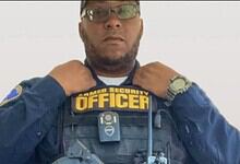 A security officer adjusting his uniform with "Security Officer" badge, wearing glasses and a watch.
