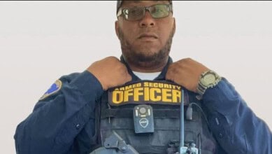 A security officer adjusting his uniform with "Security Officer" badge, wearing glasses and a watch.