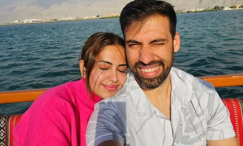 A smiling couple taking a selfie on a boat with water and mountains in the background.
