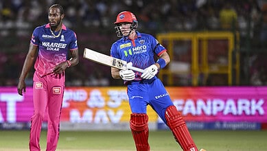 Cricket player in blue and red uniform holding bat on the field during IPL 2026 match.