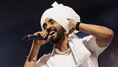 A woman wearing a white turban and traditional attire, singing passionately into a microphone on stage.