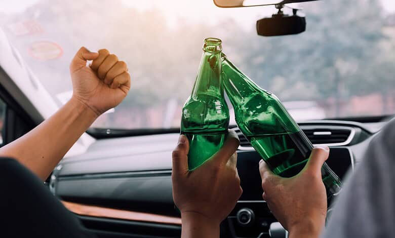 Celebrating with cheers and clinking green glass bottles inside a car during a festive occasion.