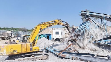 Excavator demolishing a stone crusher to address pollution concerns in RMCs.