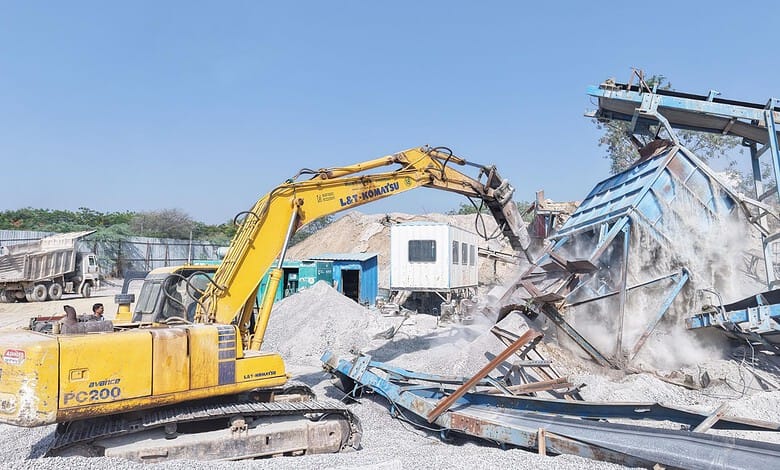 Excavator demolishing a stone crusher to address pollution concerns in RMCs.