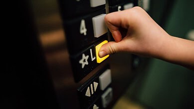 Elevator button being pressed by a child's hand in a residential building.