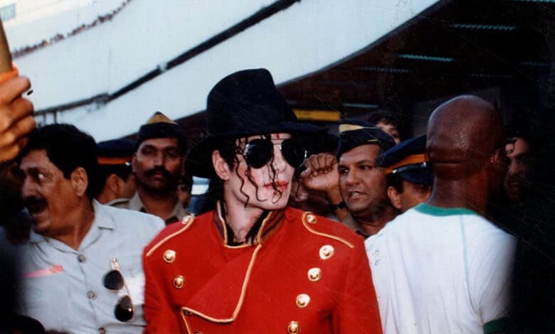 A woman dressed as Michael Jackson in a red jacket and black hat surrounded by a crowd at an event.