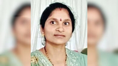 A woman in traditional Indian attire with a bindi, gold jewelry, and a light green saree, smiling softly.