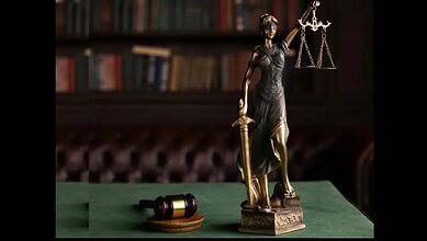 Elegant Lady Justice statue with scales and gavel on a green table in a law library setting.