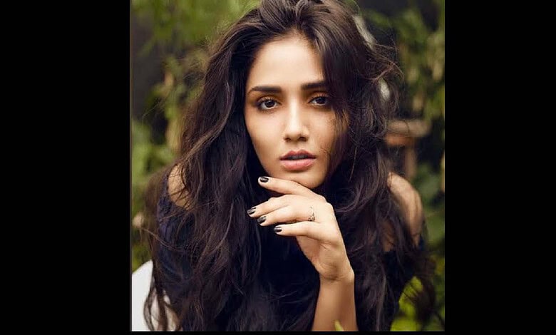 A woman with long, wavy dark hair posing outdoors in a natural setting.
