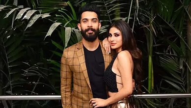 A stylish man and woman posing together at The Siasat Daily event, surrounded by lush green plants.