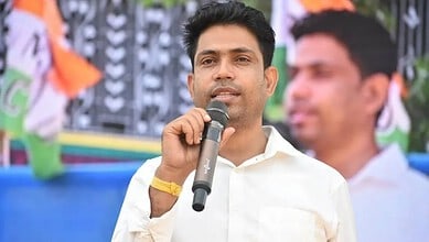 Political leader speaking at a public event in India, addressing a crowd with a microphone during a rally.