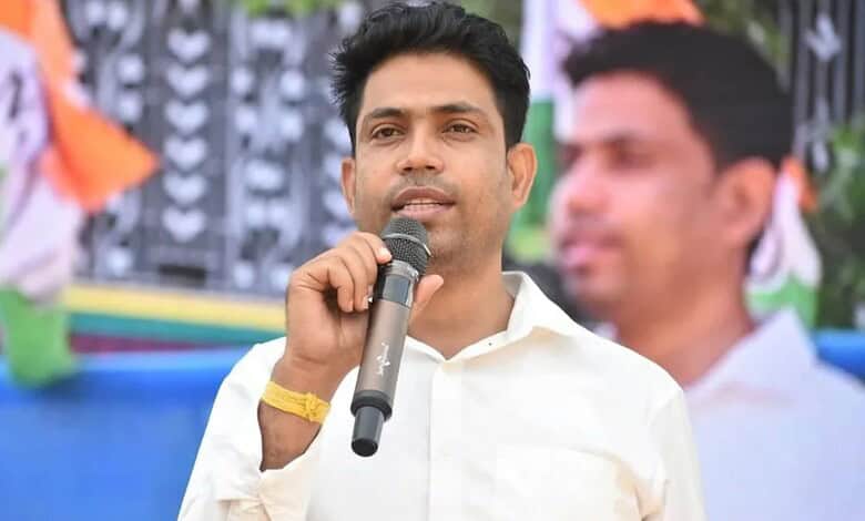 Political leader speaking at a public event in India, addressing a crowd with a microphone during a rally.