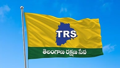 Bright yellow TRS flag with blue map outline and Telugu text, flying against a blue sky.