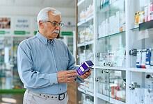 A woman in a pharmacy examining medication boxes on a shelf.