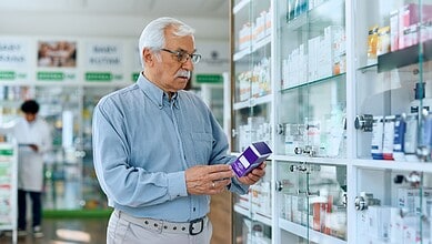A woman in a pharmacy examining medication boxes on a shelf.