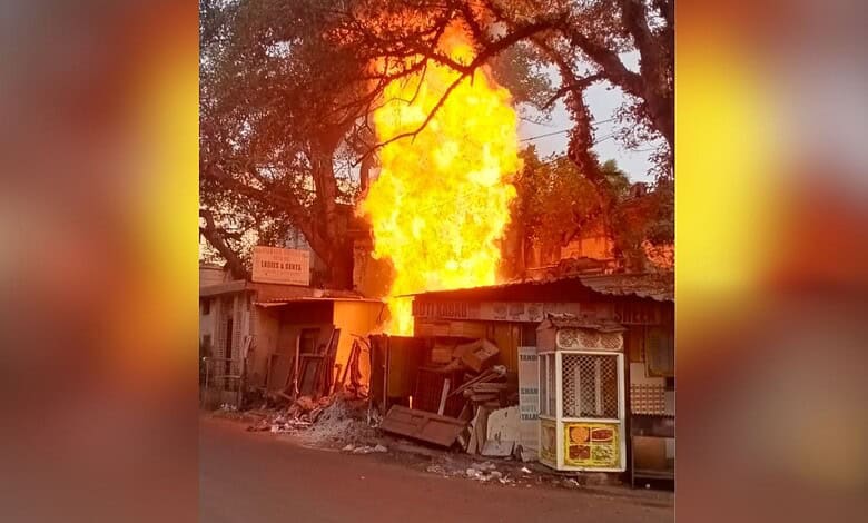 Fire erupting from a building with trees in the background during daytime, causing significant damage and.