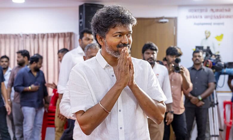 Man with folded hands at election results event, surrounded by media and supporters in Kerala.