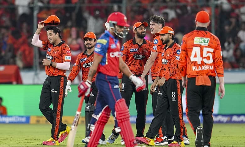 Cricket team celebrating during a match with players in orange and blue uniforms.