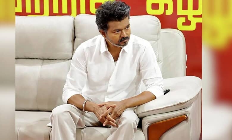 A man in a white shirt sitting on a beige sofa during a political meeting or discussion.