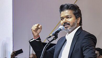 A young man in a black suit speaking passionately at a podium during a political event.