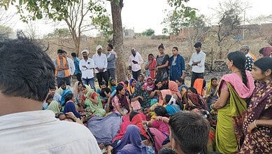 A mother and daughter with a group of women and children outdoors in a rural setting.