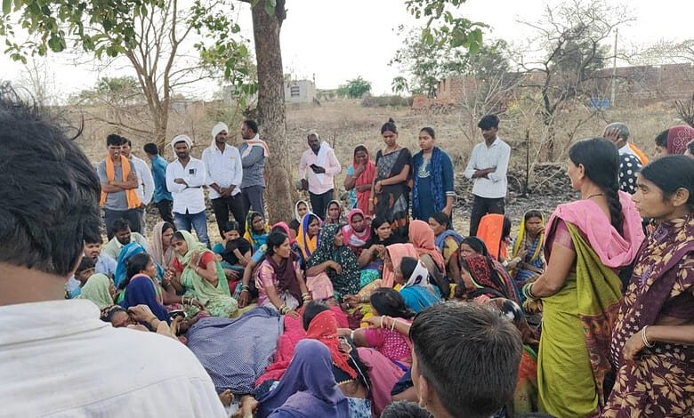 A mother and daughter with a group of women and children outdoors in a rural setting.