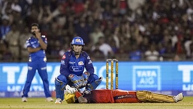 An Indian cricket player in blue uniform kneeling on the field with a cricket bat and stumps, during a ma.