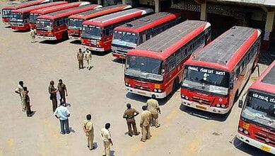 Red public buses parked in a bus depot with personnel inspecting and managing the fleet.