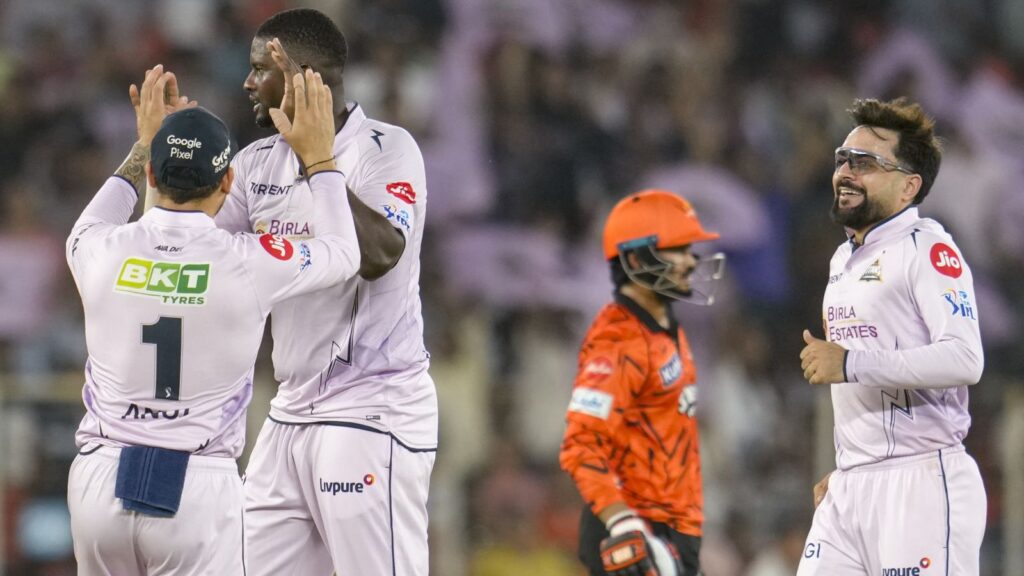 A cricket players celebrating on the field during a match, with a young wicketkeeper in orange gear in th.