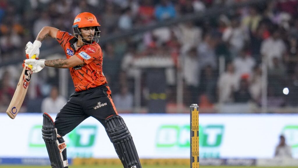 A woman cricket player in orange uniform swinging a bat during a match.