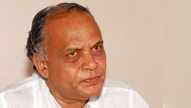 A senior man with grey hair and a serious expression, wearing a white shirt, looking to the side.