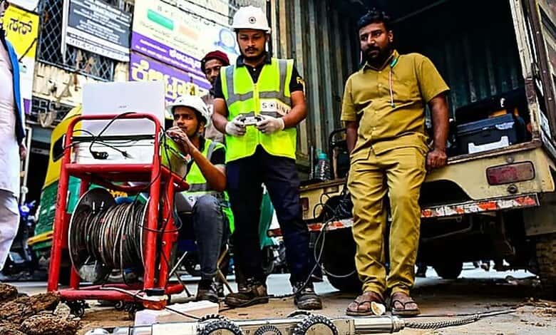 Construction workers inspecting equipment on a busy street with a cable reel and utility vehicle.