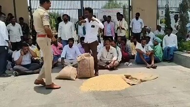 A man in white shirt and brown pants selling grains to a group of people sitting outside, with a police o.