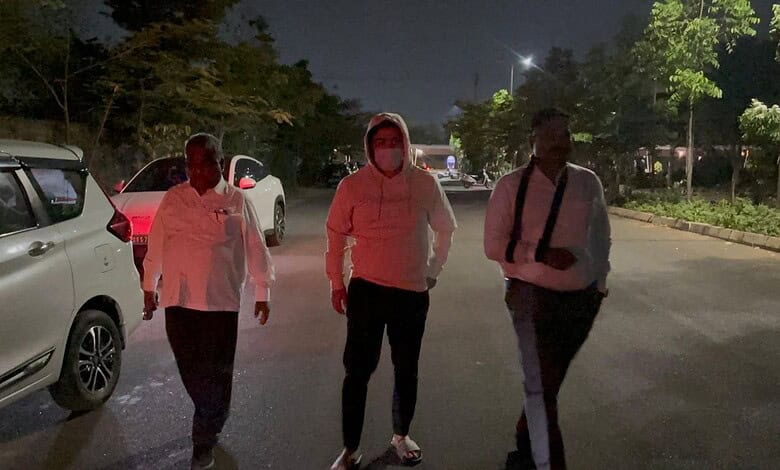 A man in a hoodie walking with two men on a street at night, illuminated by streetlights.