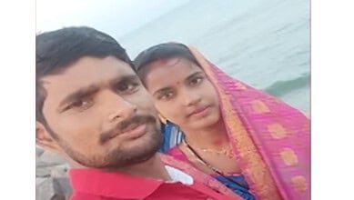 A man and woman taking a selfie near the sea, dressed in traditional Indian attire, with the ocean in the.