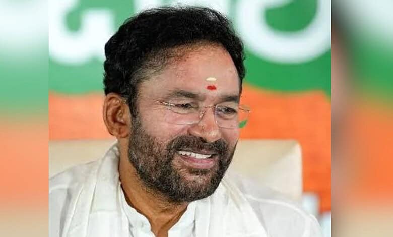 A man with glasses and a beard smiling, wearing a white traditional outfit, in front of a green and orang.