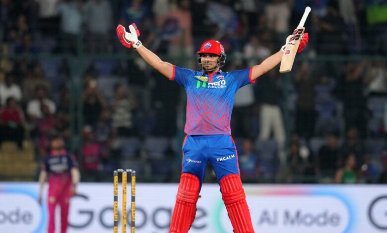 A cricket player celebrating with arms raised on the field during a match.