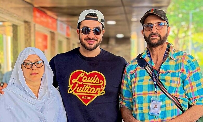 Aly Goni with his parents, smiling and dressed casually, before leaving for Haj pilgrimage, reflecting em.