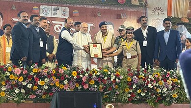 Prominent leaders and officials at a formal event with floral arrangements and a certificate presentation.