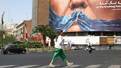 Protesters cover their mouths with a blue cloth in a busy city street amid US-Iran tensions over Hormuz.